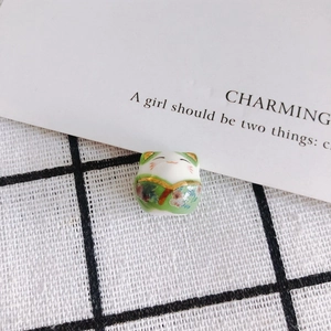 Detail of hand-painted green ceramic lucky cat bead with gold accents for DIY jewelry