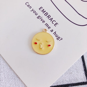 Dettaglio di un ciondolo emoji giallo con viso che bacia su un biglietto EMBRACE