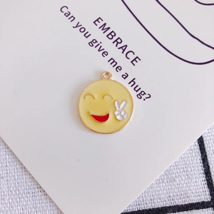 Vista macro di ciondolo emoji giallo con gesto a V su carta decorativa bianca