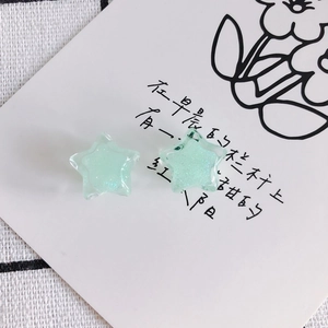 Close-up of light green star-shaped resin ear studs with subtle shimmering glitter finish