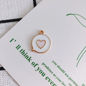 Detail of round heart charm with white enamel and golden edge on jewelry display card