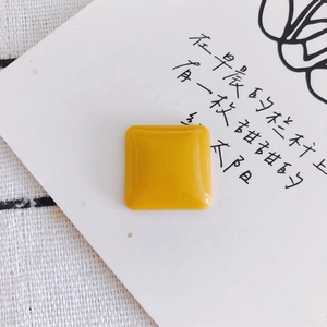 Close-up of a square yellow resin DIY charm with a glossy finish on a white artistic card
