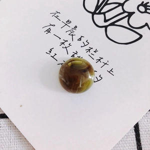 Close-up of round amber resin marble charm with green and brown swirls for DIY crafts