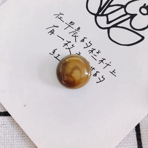 Detailed view of a round amber marble resin bead on a decorative white card with floral art