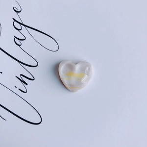 Macro detail of a heart-shaped resin accessory with pink and yellow oil painting textures