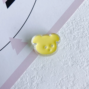 Macro shot of yellow bear-shaped resin DIY charm with three holes on artistic background