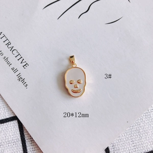 Detail view of a 20x12mm gold skull pendant with shell inlay on a white card background