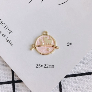Detail view of a cat-themed pink enamel pendant with gold trim and starry orbital design