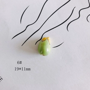 Détail d'une perle en céramique jaune et verte de 19x11mm en forme de fruit verni