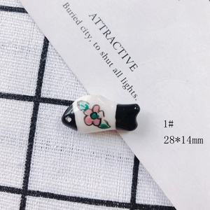 Macro detail of 28x14mm handmade ceramic fish pendant with painted pink flower motifs