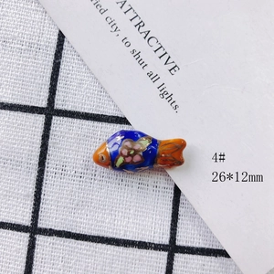Detail view of 26x12mm handmade blue ceramic fish bead with floral pattern and orange fins