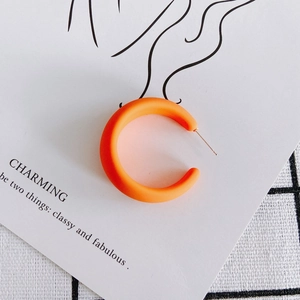 Macro shot of matte orange C-shaped acrylic hoop earrings on artistic jewelry card
