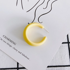 Close-up of matte yellow C-shaped acrylic earring on minimalist background