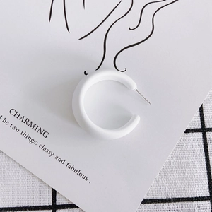Macro shot of white matte acrylic C-shaped hoop earring with metal pin on aesthetic backdrop