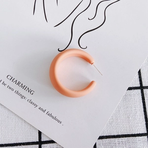 Macro detail of apricot matte acrylic C-shaped hoop earring on a minimalist card