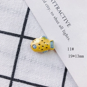 Macro shot of yellow ceramic fish bead with blue fins and size label 19x13mm