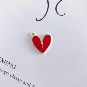Dettaglio di un ciondolo a cuore rosso con bordo dorato a perline e anello in metallo