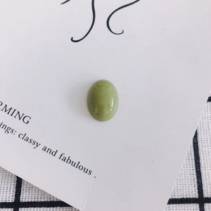 Macro shot of oval green acrylic resin bead on elegant white card and checkered background