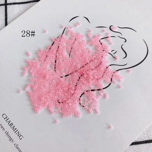 Detailed view of 2mm pink translucent glass seed beads artfully arranged on paper
