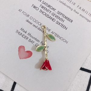 Detailed close-up of a red enamel rose flower charm with green leaves and gold stem