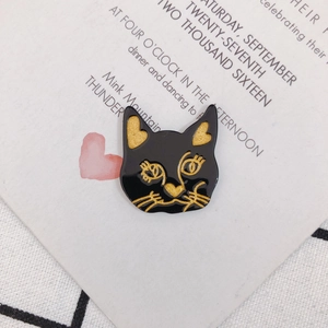 Détail d'une broche chat en émail noir avec contours dorés sur carte d'invitation