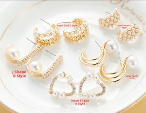 Detailopname van vijf elegante gouden oorbellen met parels en kristallen op een wit keramisch bord