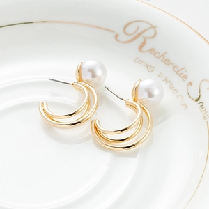 Close-up van elegante goudkleurige gelaagde oorringen met witte parels op een schaaltje