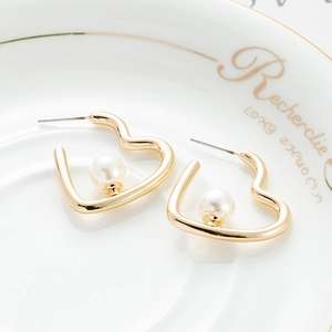 Elegante gouden hartvormige oorbellen met parels op een decoratief bord gepresenteerd