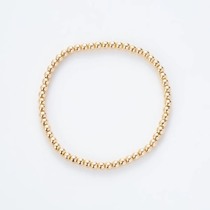Vista detallada de una pulsera elástica minimalista de cuentas doradas sobre blanco