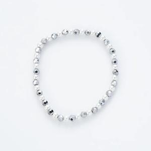 Detalle de perlas blancas brillantes y cuentas plateadas facetadas en una pulsera elástica