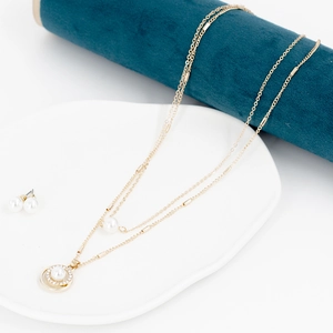 Detail einer doppelten Goldkette mit Perlenanhängern und passenden Perlenohrsteckern