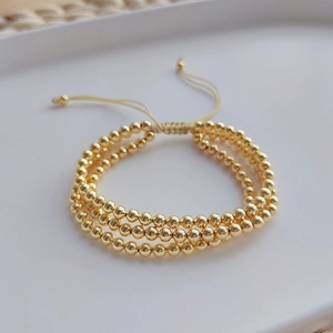Drielagige gouden kralenarmband met verstelbaar trekkoord op een wit dienblad
