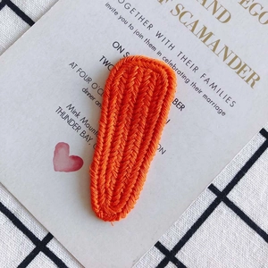 Macro detail of orange knit hair clip featuring a textured herringbone weave pattern