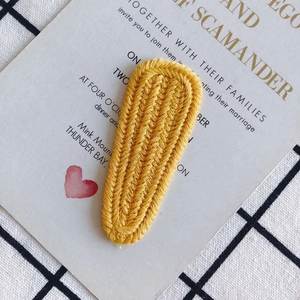 Detailed macro view of yellow knitted hair clip with 3D braided texture and warm handmade feel
