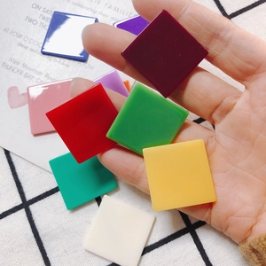 Colorful square resin charms for DIY jewelry making held against a checkered background
