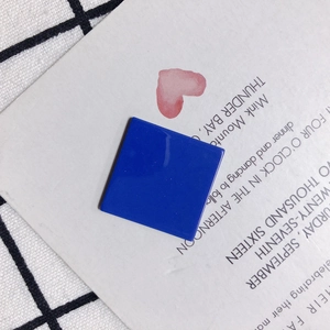 Macro shot of square Klein blue resin jewelry piece with high-gloss finish on a grid fabric