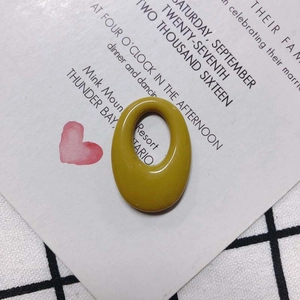 Close-up of a mustard yellow oval resin charm on a decorative white card and plaid fabric