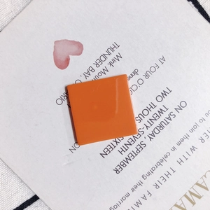 Close-up of a bright orange square resin charm on an artistic paper background