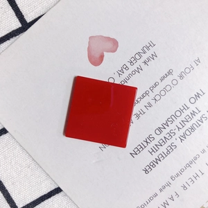 Flat lay of red square resin accessory with glossy finish on aesthetic display card