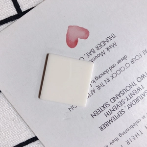 Detail shot of square cream-white resin charm for DIY jewelry on textured background