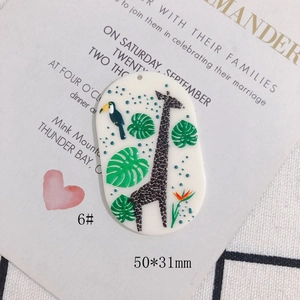 Macro detail of acrylic oval giraffe and toucan charm with tropical leaves pattern