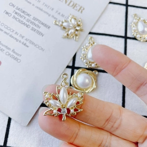 Golden maple leaf pendant with white pearls and zircons shown in a hand-held view