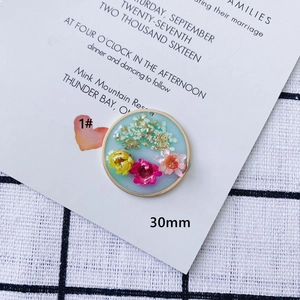 Dettaglio di un ciondolo in resina da 30mm con fiori secchi colorati e foglie d'oro