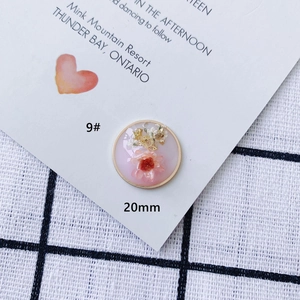 Dettaglio ciondolo rotondo in resina da 20mm con fiori secchi rosa e farfalla dorata