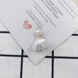 Close-up of elegant white fabric flower charm with pearl detail and golden metal hook