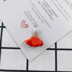 Macro shot of orange fabric flower charm with white pearl and gold filigree cap detail