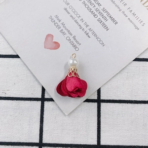 Macro view of a dark red fabric petal charm with pearl and golden filigree cap