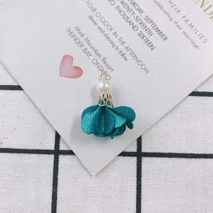 Macro view of handmade peacock green fabric flower charm with pearl and golden base