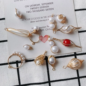 Detail of DIY jewelry charms with gold wire wrapped pearls and red beads on white cloth