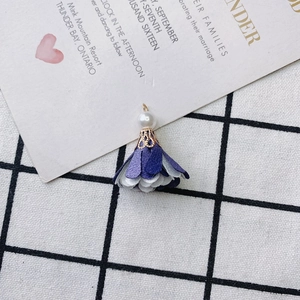 Detail of fabric flower charm with purple petals, gold metal cap, and white pearl bead